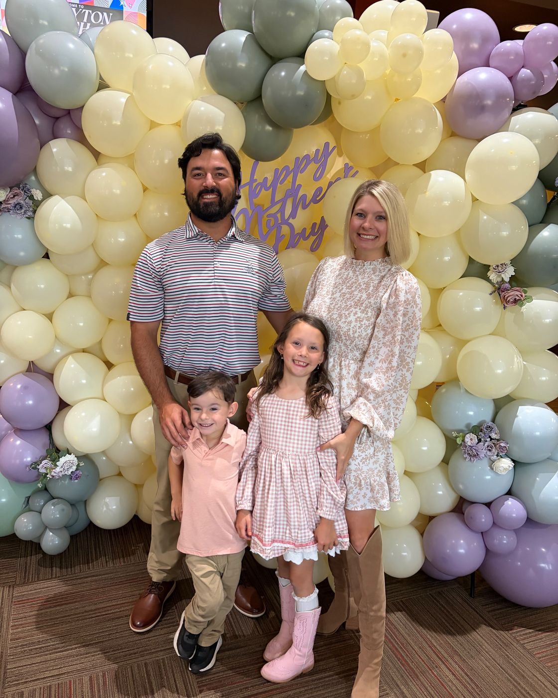 Sara with her husband and two children in front of a pastel balloon arch on Mother's Day